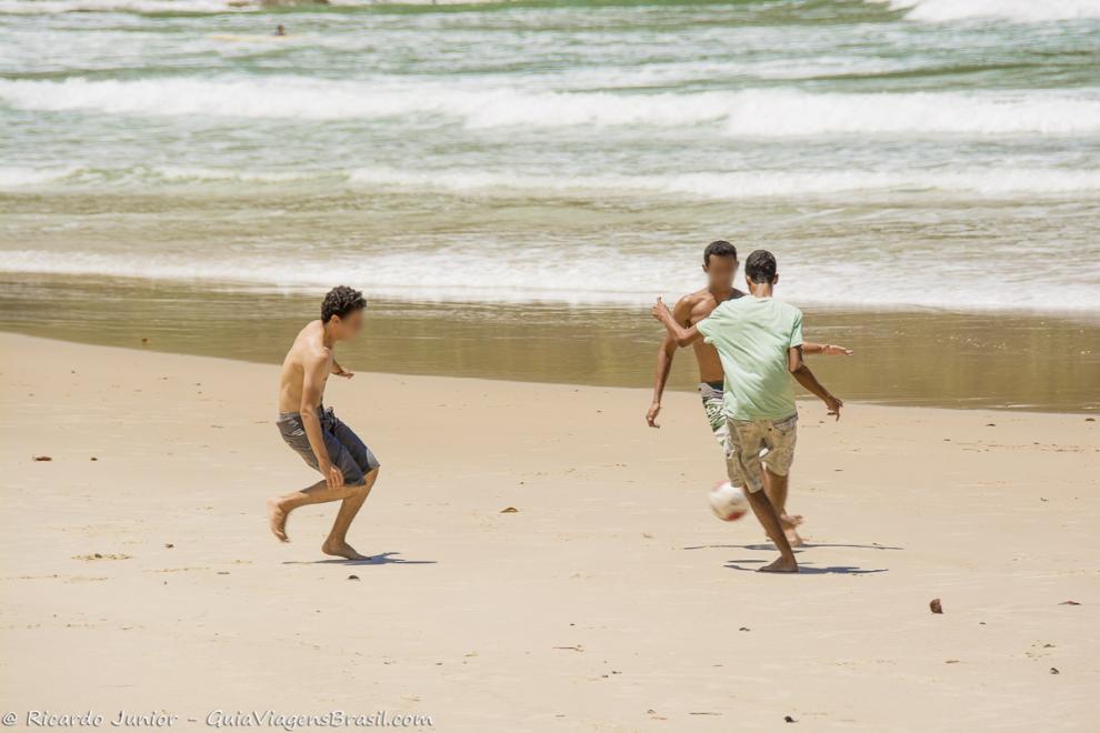 Imagem de meninos jogando futebol na beira do mar.